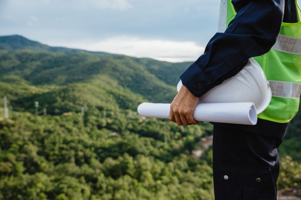 Engineer Holding Hardhat and Certification With Green Mountains In The Background